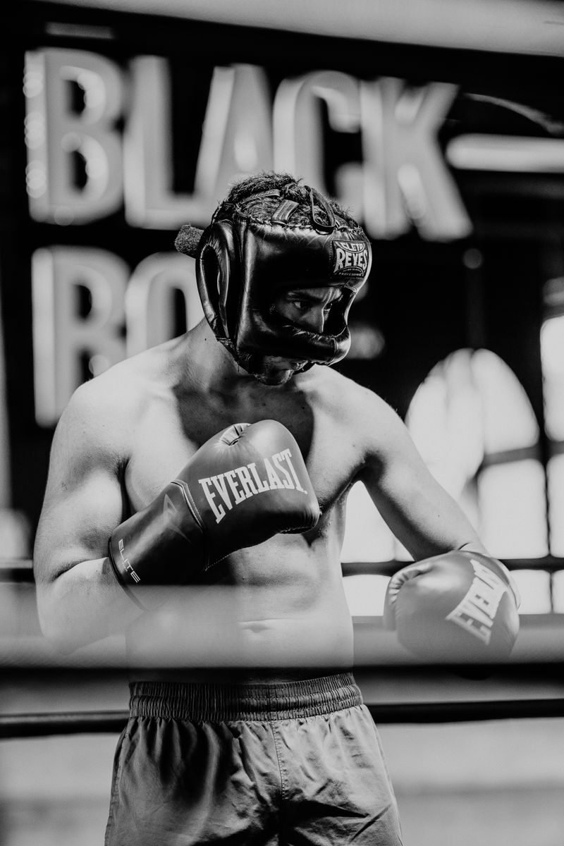 A focused boxer in gloves and headgear captured in a dramatic black and white portrait.